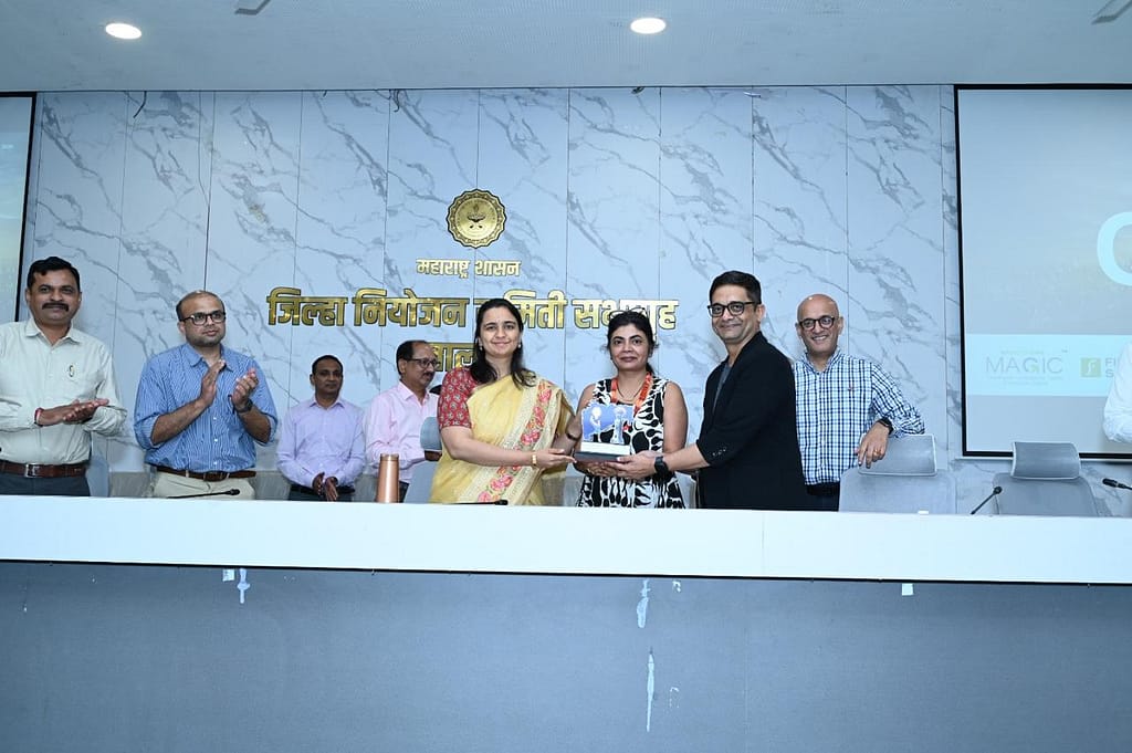 WhatsApp Image 2026-02-09 at 181534 - NewsNation Online A group of individuals at a formal gathering, celebrating an award presentation. The scene features a woman in a yellow sari receiving a trophy, while several others, including men in shirts and formal attire, applaud in the background. The backdrop includes a decorative wall with a logo and the words in Marathi.